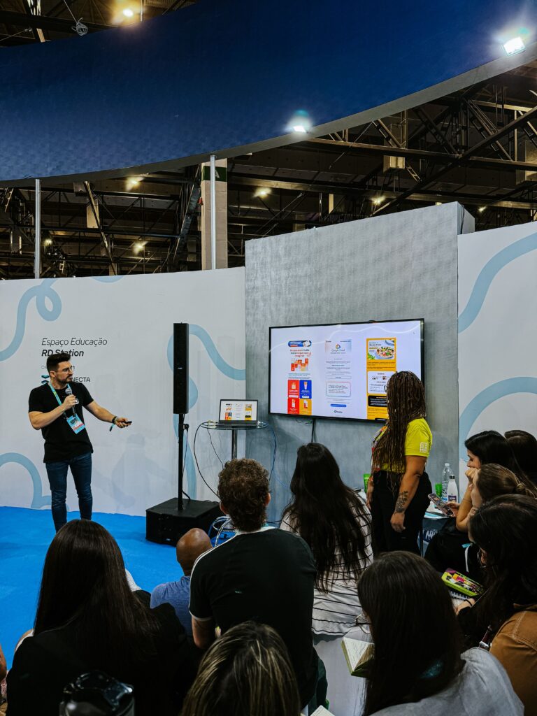 Emerson Stempim, de camiseta preta e credencial do RD Summit 2024,  apontando na direção de uma TV, com uma apresentação de Power Point, na sua palestra Copywriting pode mudar o jogo em campanhas?