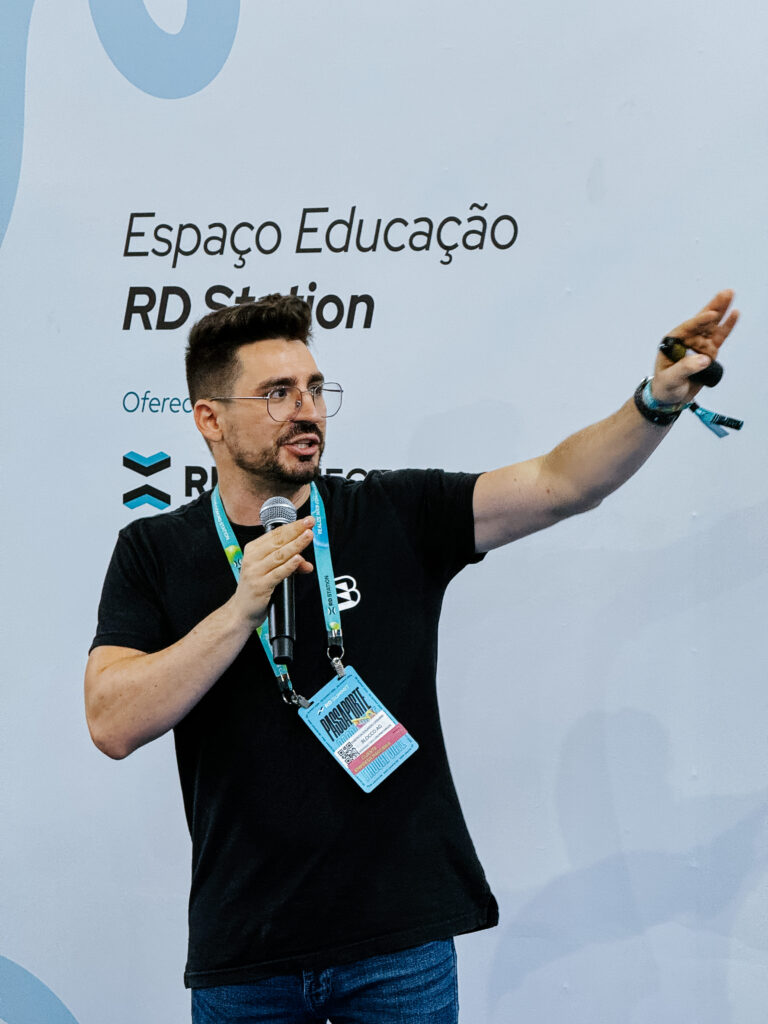 Emerson Stempim, de camiseta preta e credencial do RD Summit 2024, olhando para o lado e apontando na sua palestra Copywriting pode mudar o jogo em campanhas?