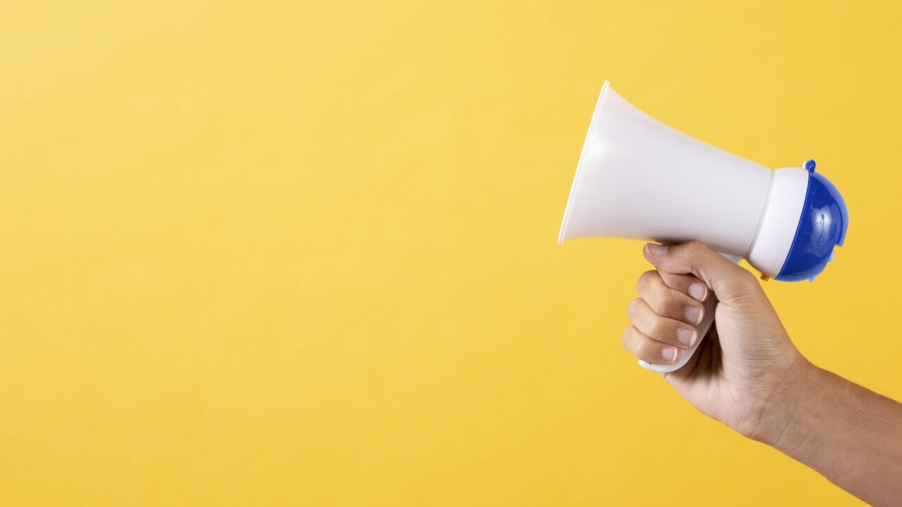 Fundo amarelo com uma mão segurando um megafone