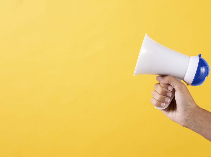 Fundo amarelo com uma mão segurando um megafone
