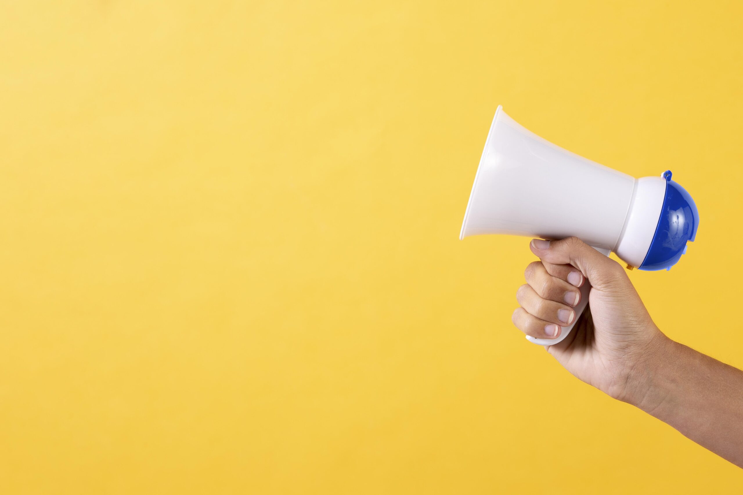Fundo amarelo com uma mão segurando um megafone