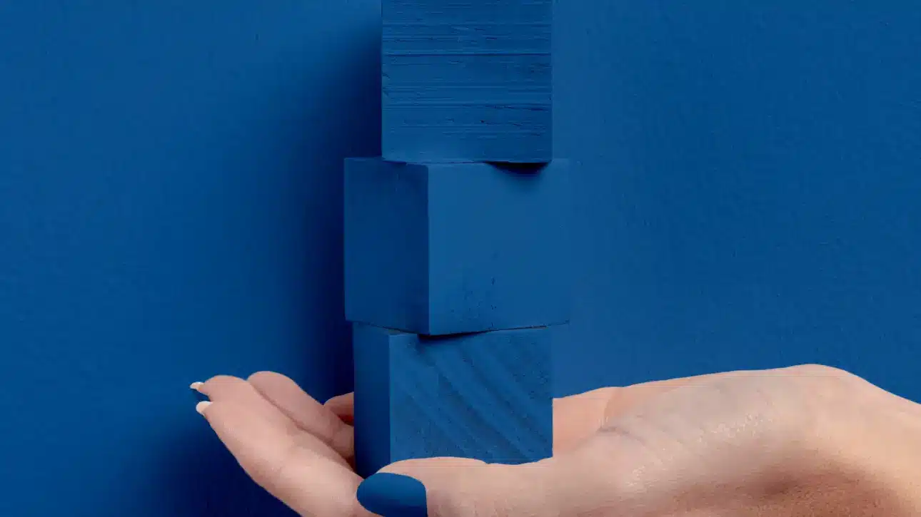 Posicionamento de marca representado por uma mão segurando três blocos azuis empilhados sobre fundo azul.
