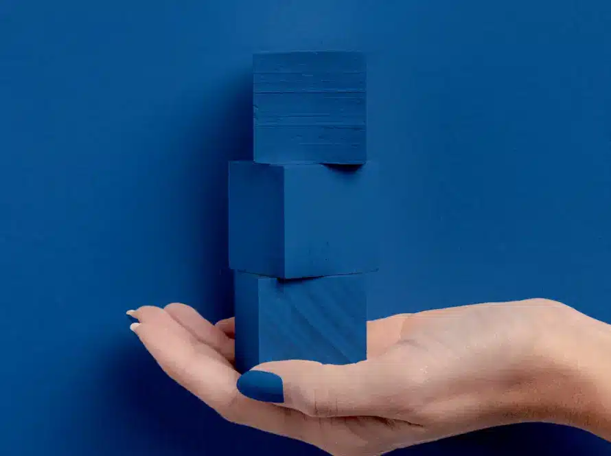 Posicionamento de marca representado por uma mão segurando três blocos azuis empilhados sobre fundo azul.