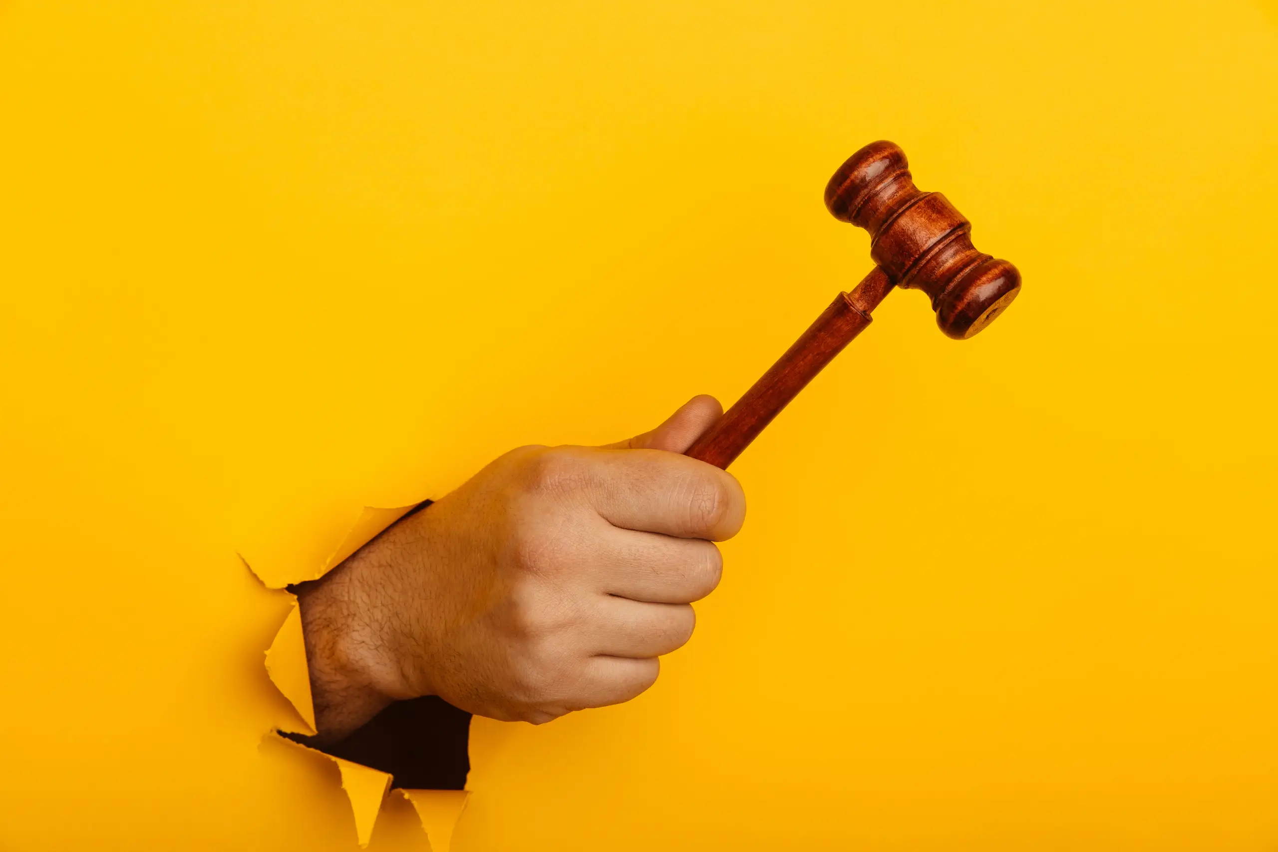 mão segurando um martelo de juiz através de um rasgo em fundo amarelo, representando o leilão de anúncios e como funciona no Meta Ads